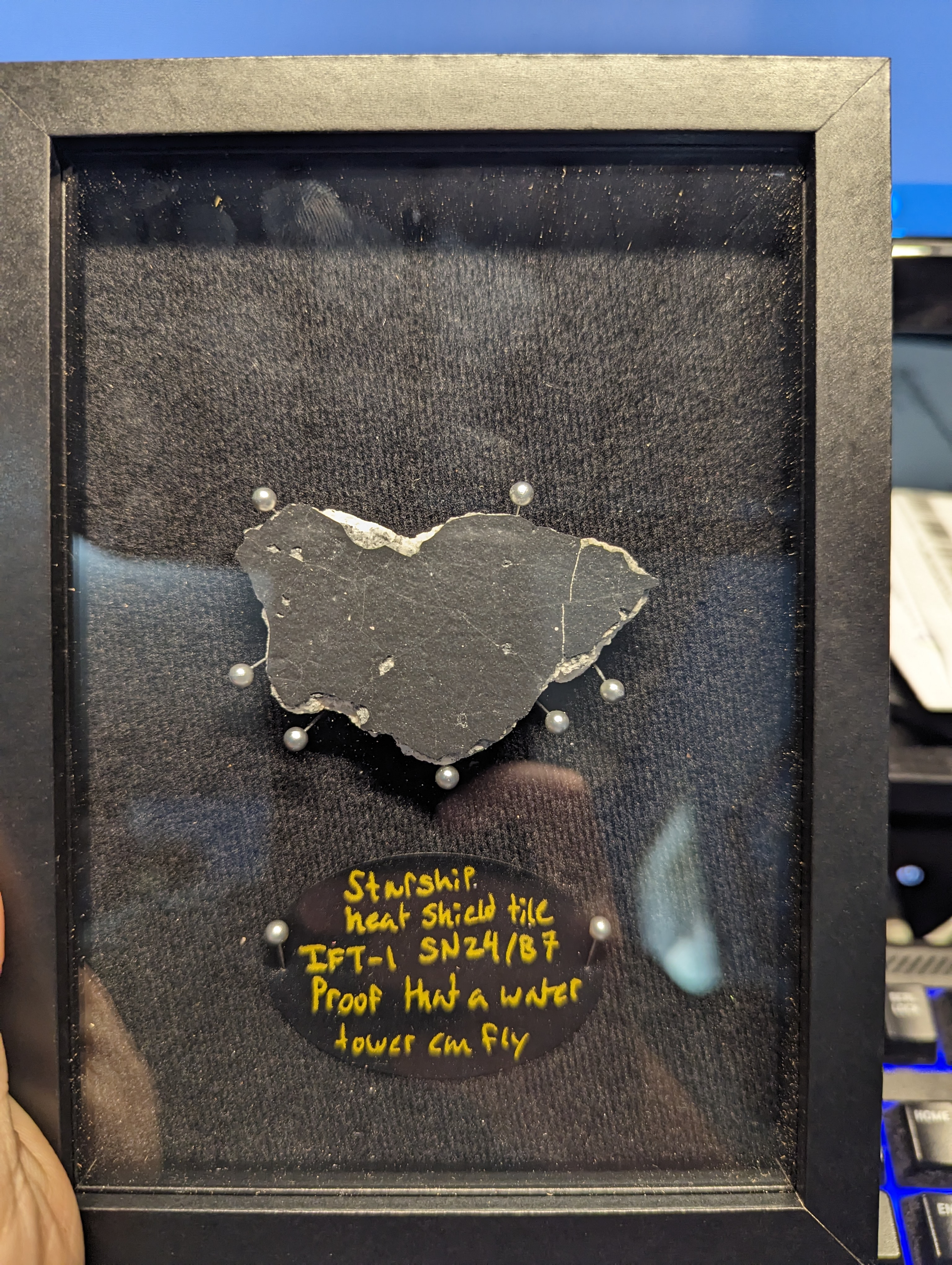 The fragment in its shadow box. The label reads, “Proof that a water tower can fly.”